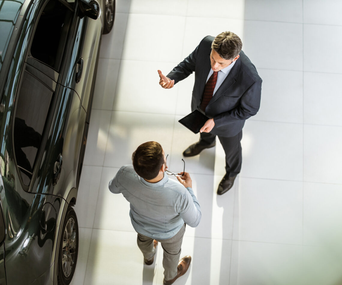 Above view of car salesperson talking to his customer in a showroom.